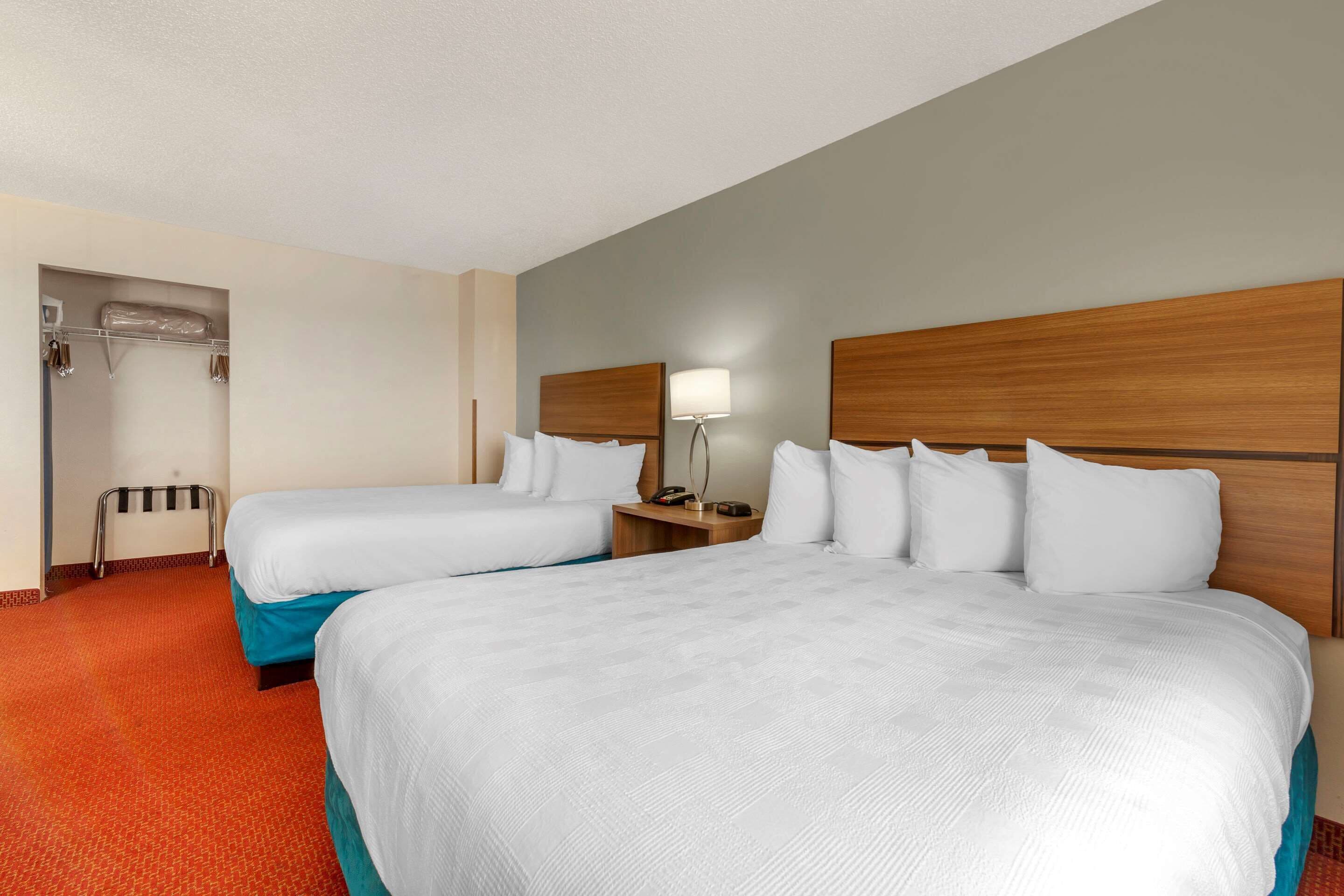A hotel room with two beds, a wooden headboard, a nightstand with a lamp, and a coat rack.