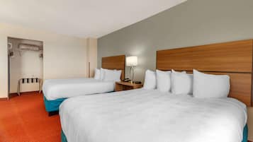 A hotel room with two beds, a wooden headboard, a nightstand with a lamp, and a coat rack.