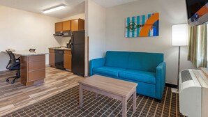 A compact hotel room with a kitchenette, a blue sofa, a small table, and a TV. - MainStay Suites Dubuque at Hwy 20 (Dubuque)