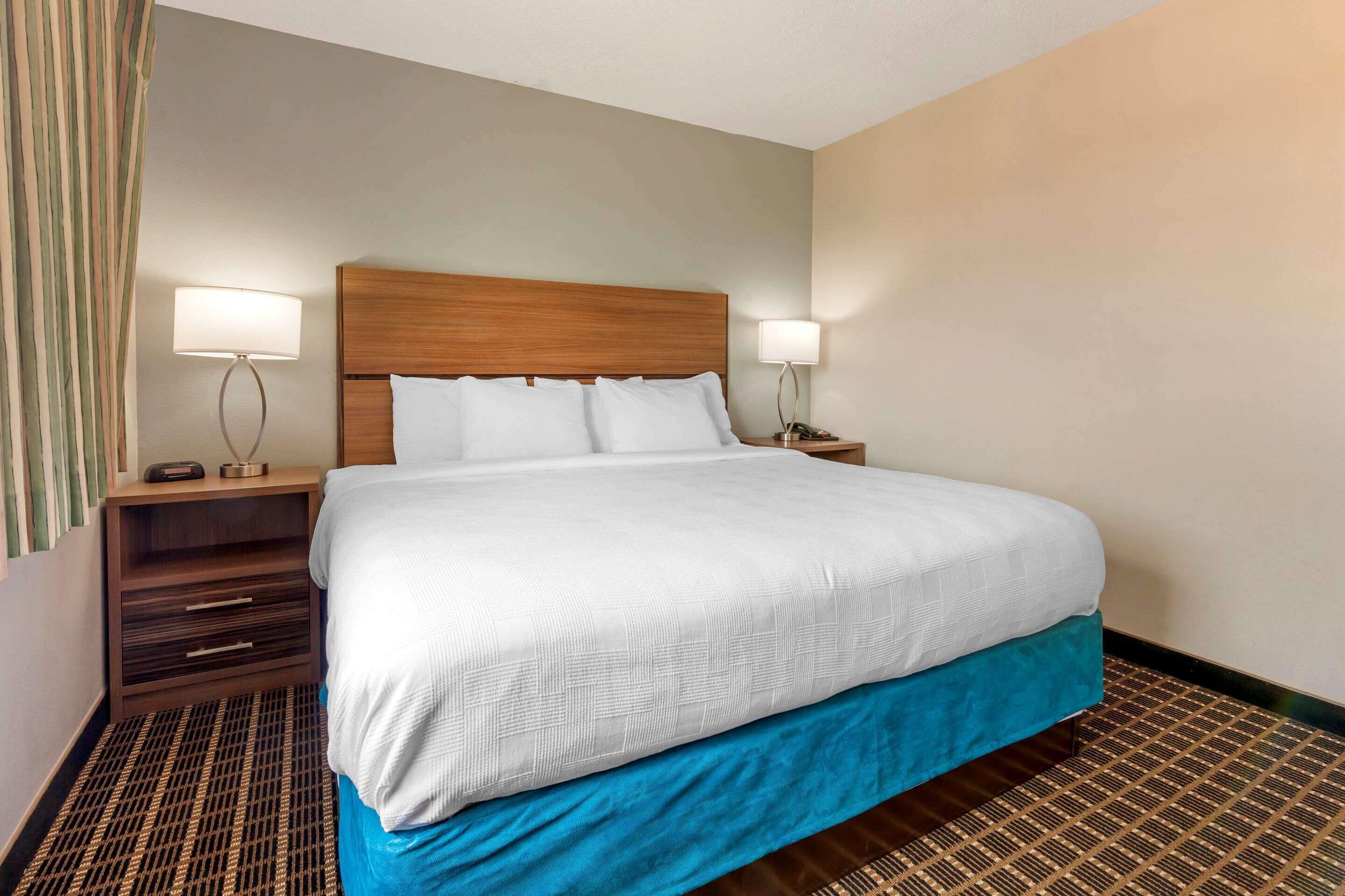 A hotel room with a large bed, two bedside tables with lamps, a wooden headboard, and a patterned floor.