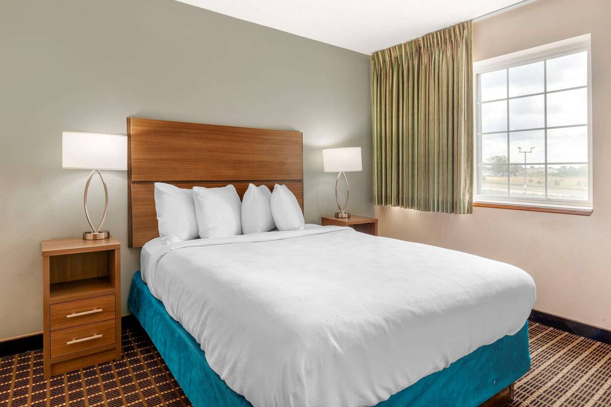 A hotel room with a large bed, two bedside tables, a window with curtains, and a view of the outdoors.
