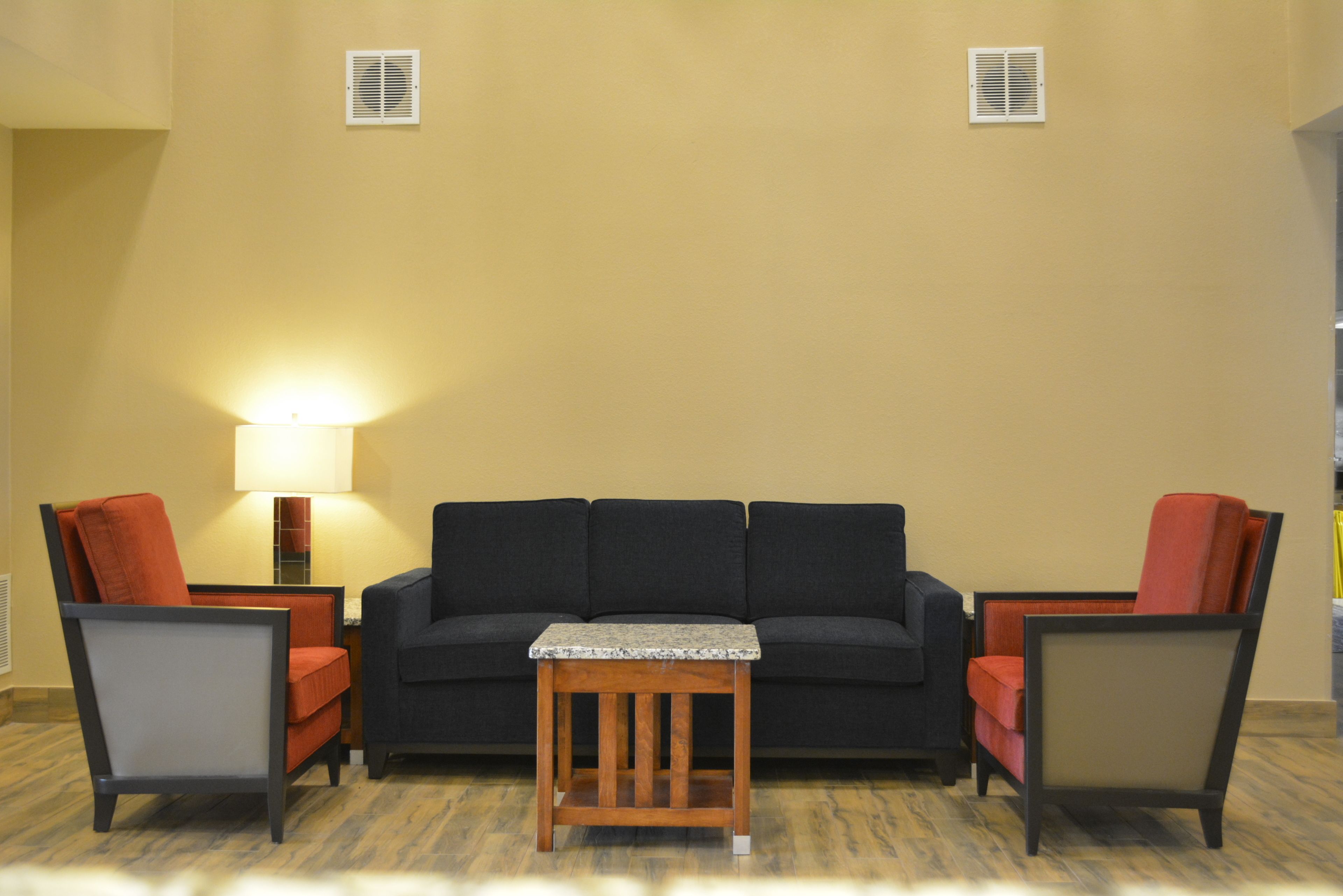 Een woonkamer met een donkere bank, twee fauteuils, een klein houten tafeltje en een lamp.