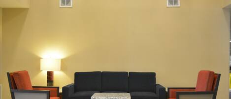 A living room with a dark sofa, two armchairs, a small wooden table, and a lamp.