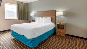A hotel room with a large bed, two bedside tables, a window with curtains, and a patterned carpet. - MainStay Suites Dubuque at Hwy 20 (Dubuque)