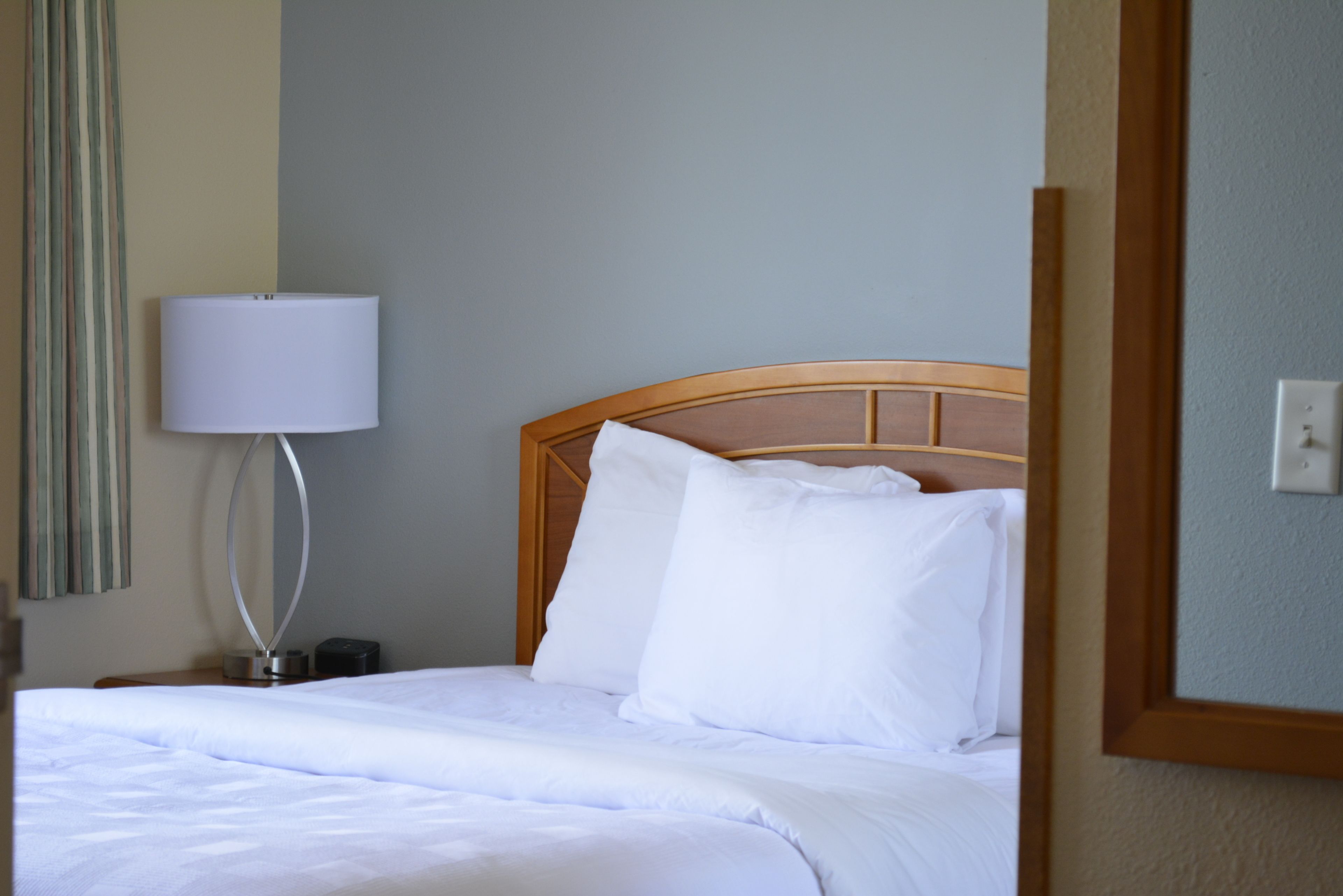A neatly made bed with white linens and pillows, a bedside lamp, and a wooden headboard.