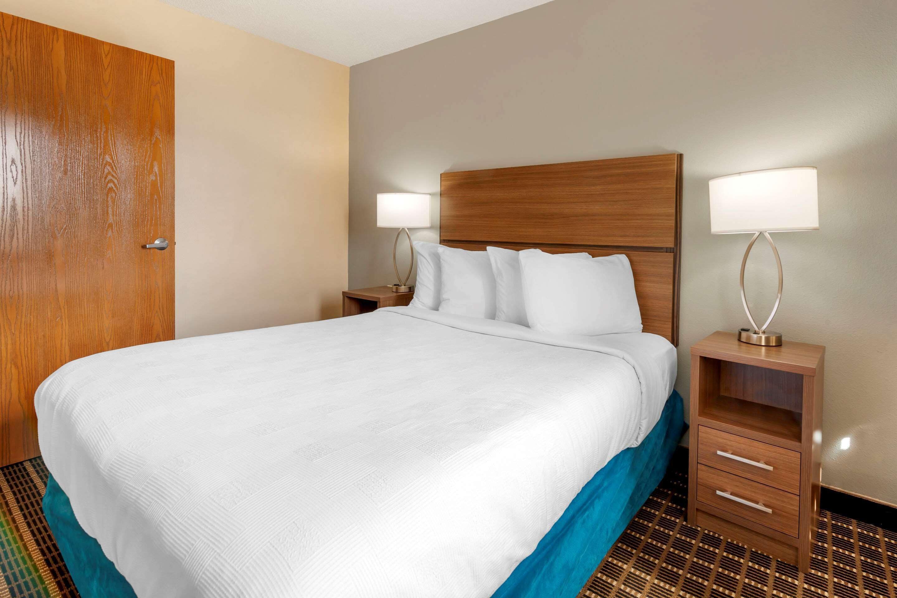 A hotel room with a large bed, two bedside tables with lamps, a wooden headboard, and a patterned floor.