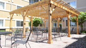 A covered outdoor seating area with tables and chairs, wooden beams, and a building with multiple windows in the background. - MainStay Suites Dubuque at Hwy 20 (Dubuque)