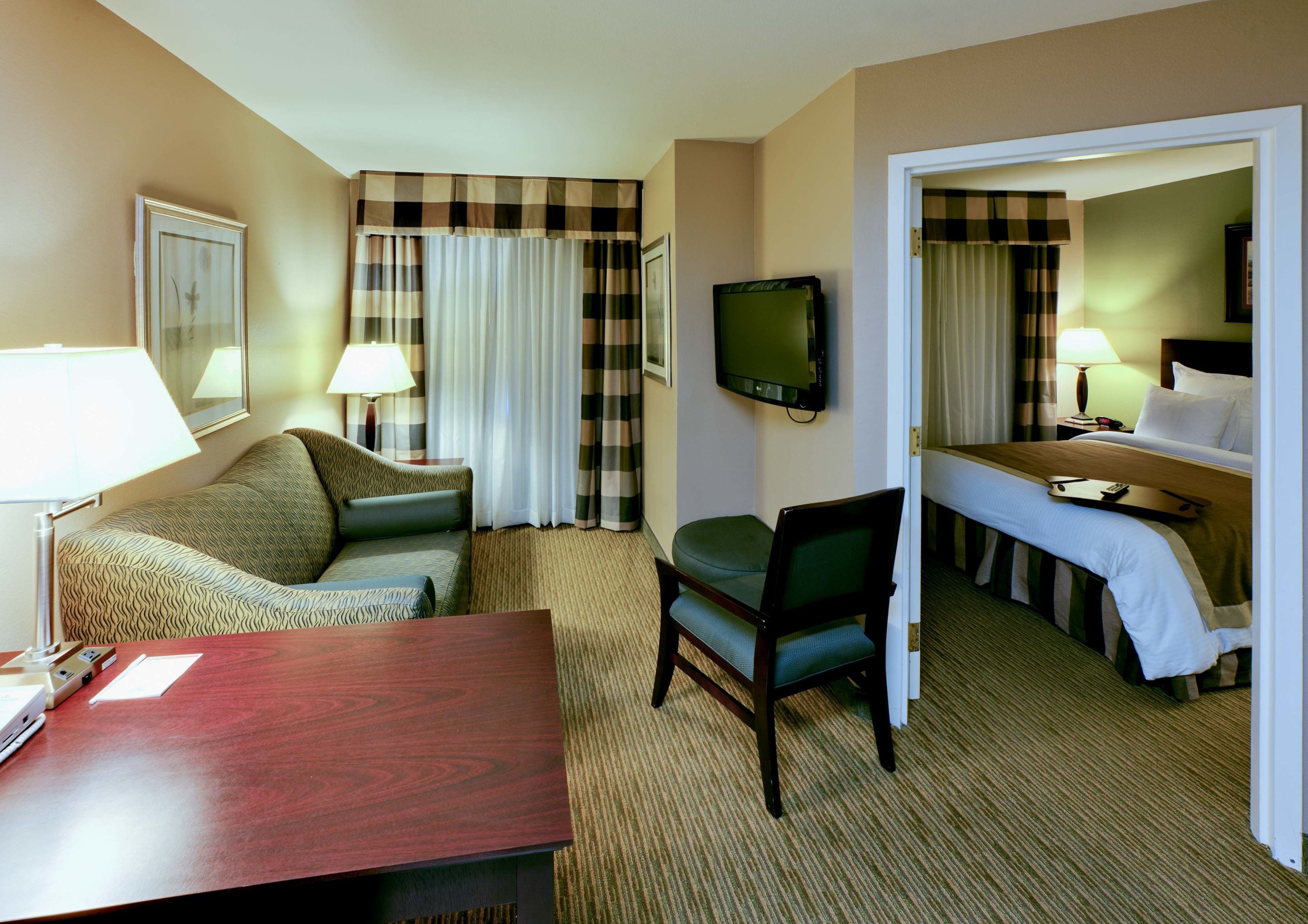 A hotel room with a bed, a desk, a chair, a television, and a window with curtains.