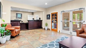 A reception area with a desk, chairs, potted plants, and a glass door leading outside. - MainStay Suites Addison-Dallas (Addison)