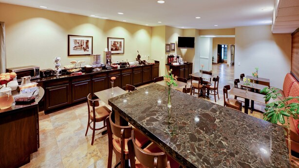 A spacious kitchen with a large marble island, wooden chairs, and a dining area with a bench. - MainStay Suites Addison-Dallas (Addison)