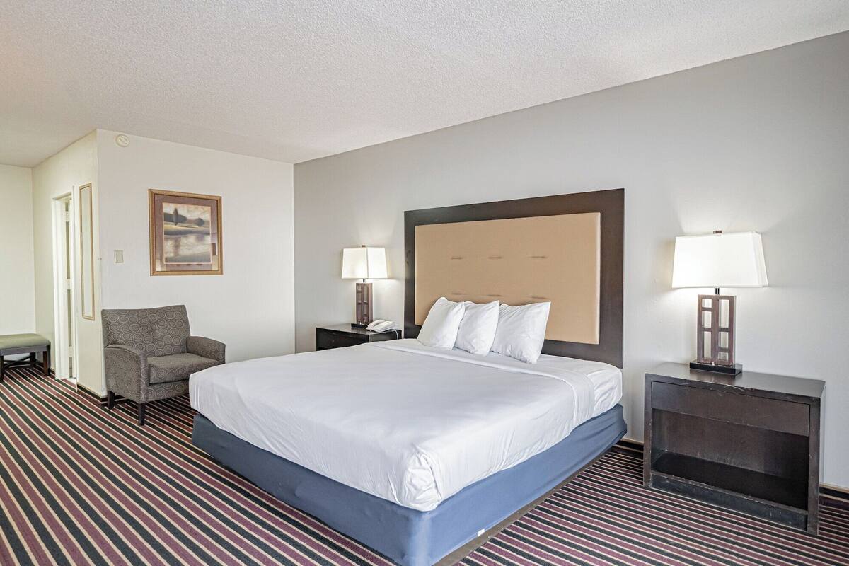 A hotel room with a large bed, two bedside tables with lamps, a chair, and a painting on the wall.