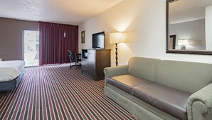 A hotel room with a bed, a sofa, a desk with a computer, a lamp, and a large mirror. - Motel 6 Pocatello, ID (Pocatello)