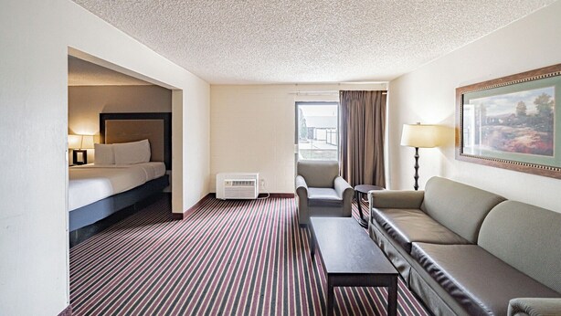 A hotel room with a bed, a sofa, a small table, a chair, a lamp, and a painting on the wall. - Motel 6 Pocatello, ID (Pocatello)