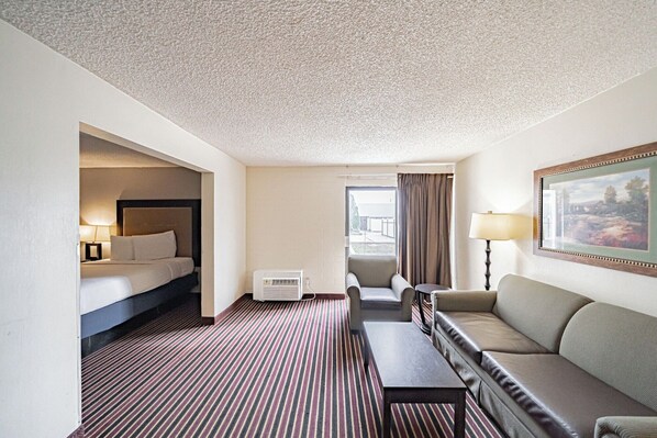 A hotel room with a bed, a sofa, a small table, a chair, a lamp, and a painting on the wall. - Motel 6 Pocatello, ID (Pocatello)