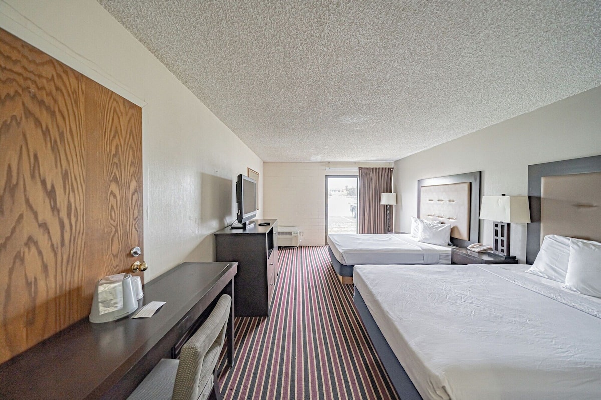 A hotel room with two beds, a desk, a TV, and a window with curtains.