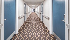 A hotel corridor with patterned carpet, blue doors, and white walls. - Motel 6 Pocatello, ID (Pocatello)