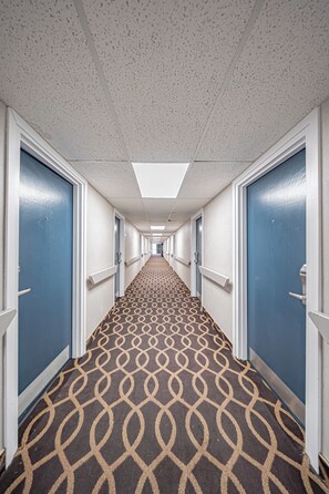 A hotel corridor with patterned carpet, blue doors, and white walls. - Motel 6 Pocatello, ID (Pocatello)
