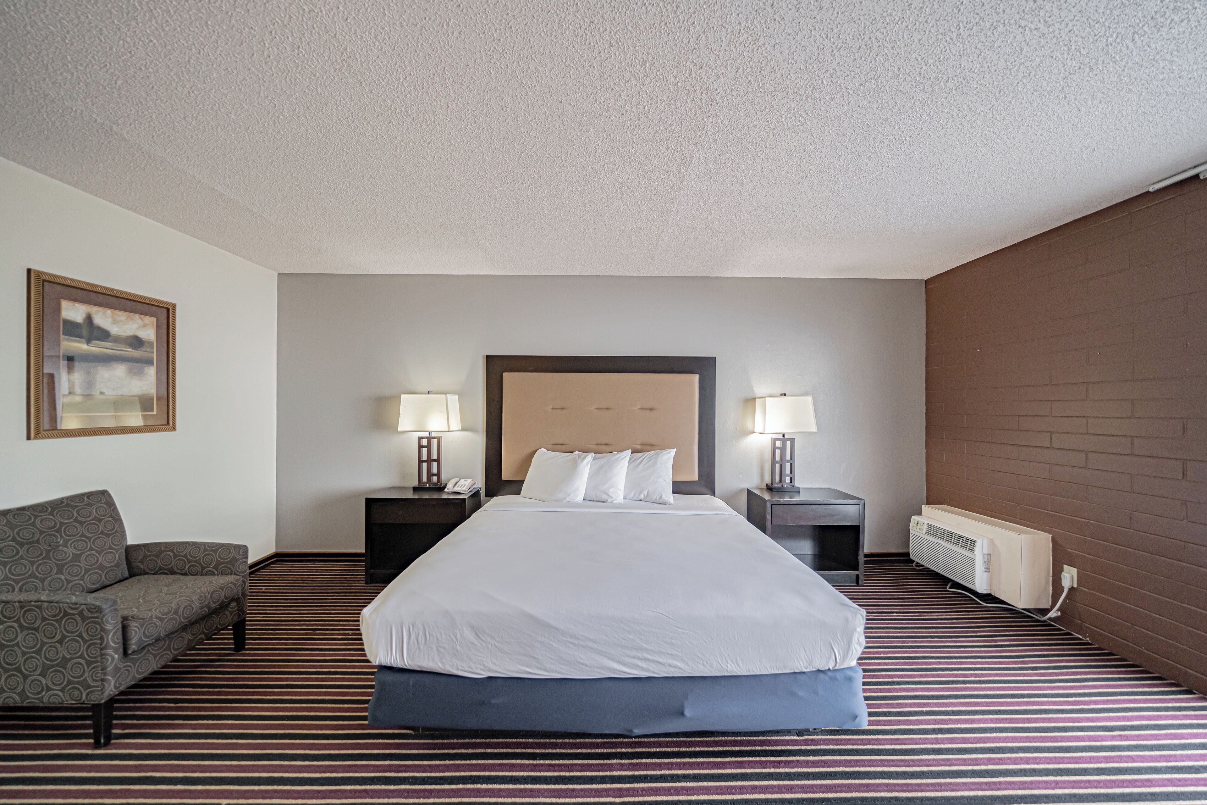 A hotel room with a large bed, two bedside tables with lamps, a sofa, and a radiator.