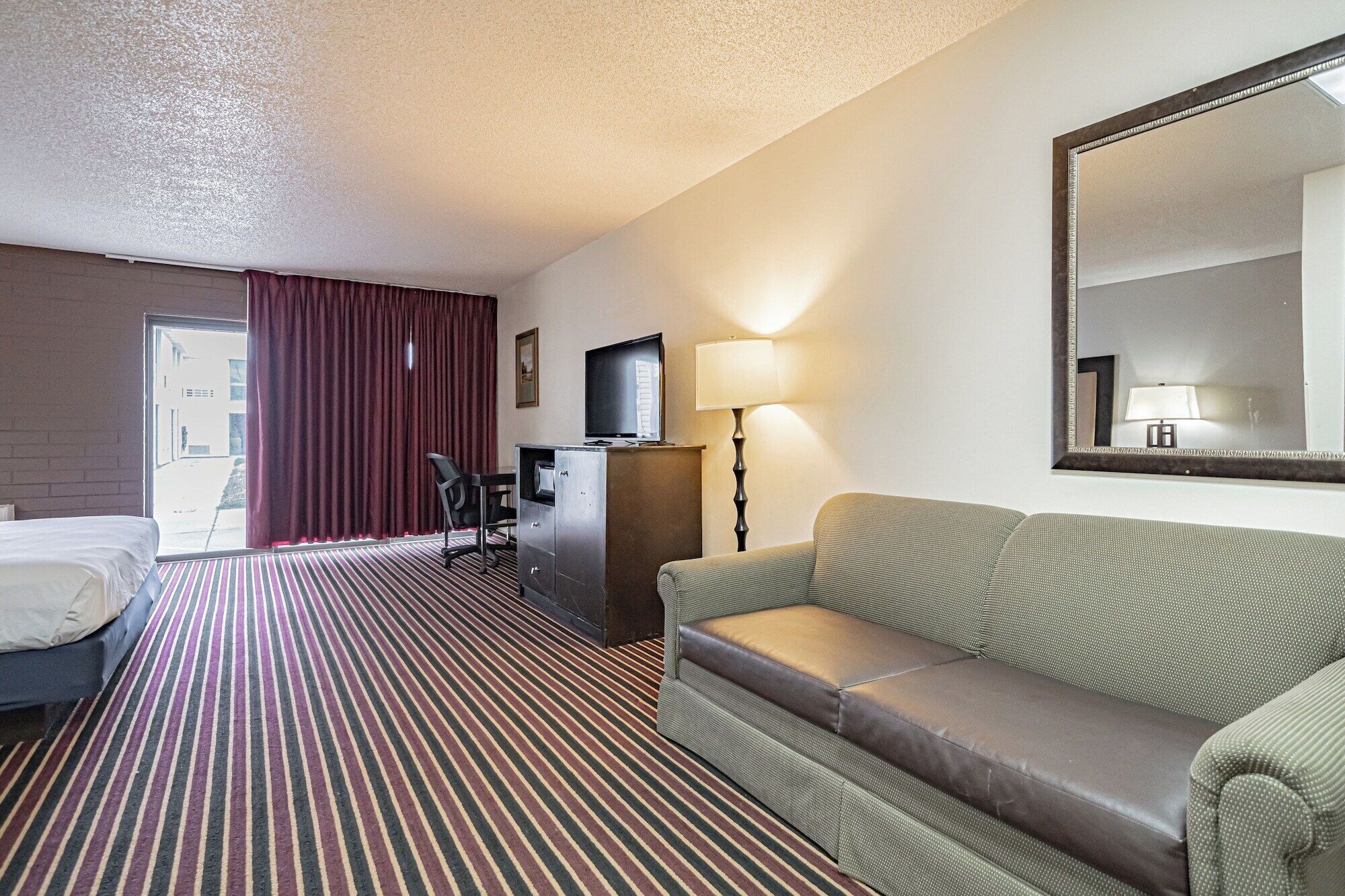 A hotel room with a bed, a sofa, a desk with a chair, a lamp, and a television.