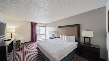 Habitación de hotel con una cama grande, un escritorio con lámpara, un televisor y una ventana con cortinas.