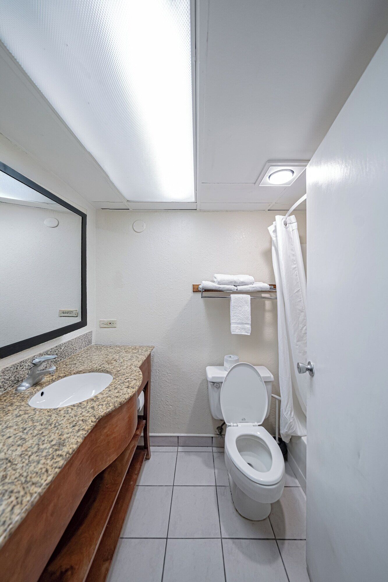 A bathroom with a granite countertop sink, a mirror, a toilet, and a shower curtain.