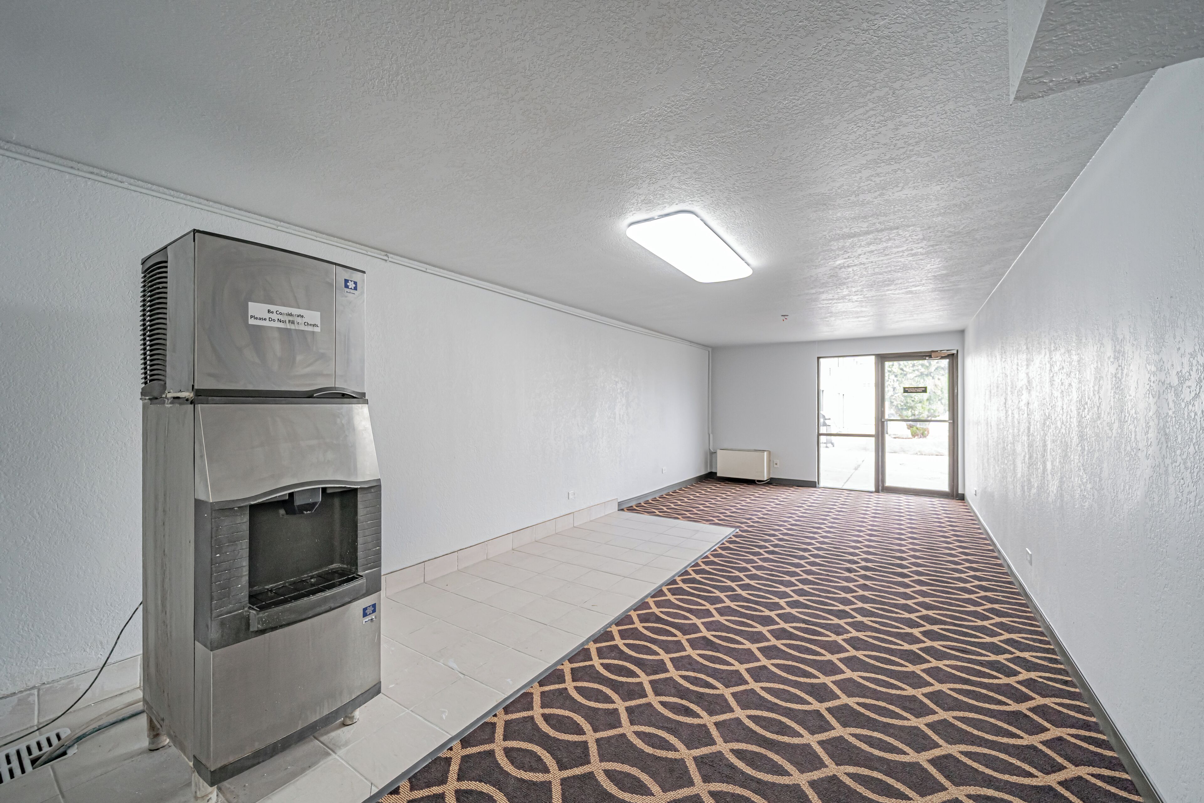 A hallway with a patterned carpet, a water dispenser, and a door leading to an outdoor area.