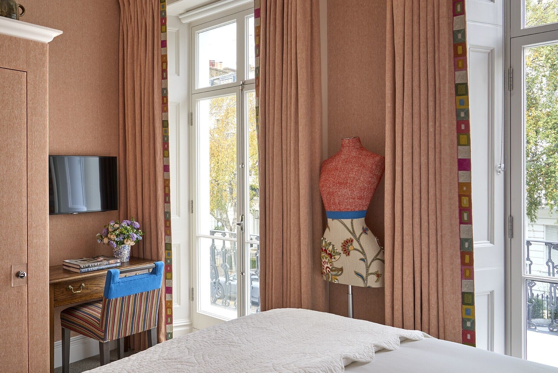 A bedroom with a bed, a desk with a chair, a TV, and a mannequin.