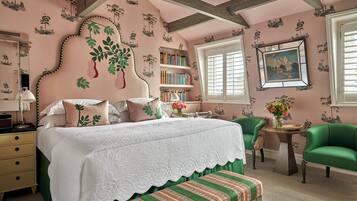 Un dormitorio con una cama grande, un sillón verde, una mesita con un florero y una estantería.