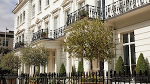 Un edificio blanco con balcón de hierro forjado negro y un árbol grande al frente.
