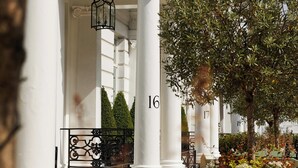 Un edificio blanco con columnas, números 16 y 17, y una planta grande en maceta con flores.