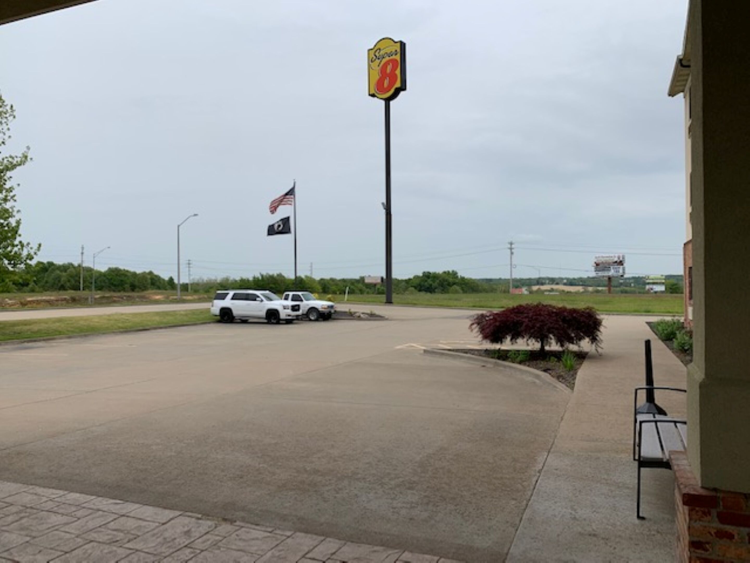 A parking lot with a white SUV, a sign for a business, and an American flag.