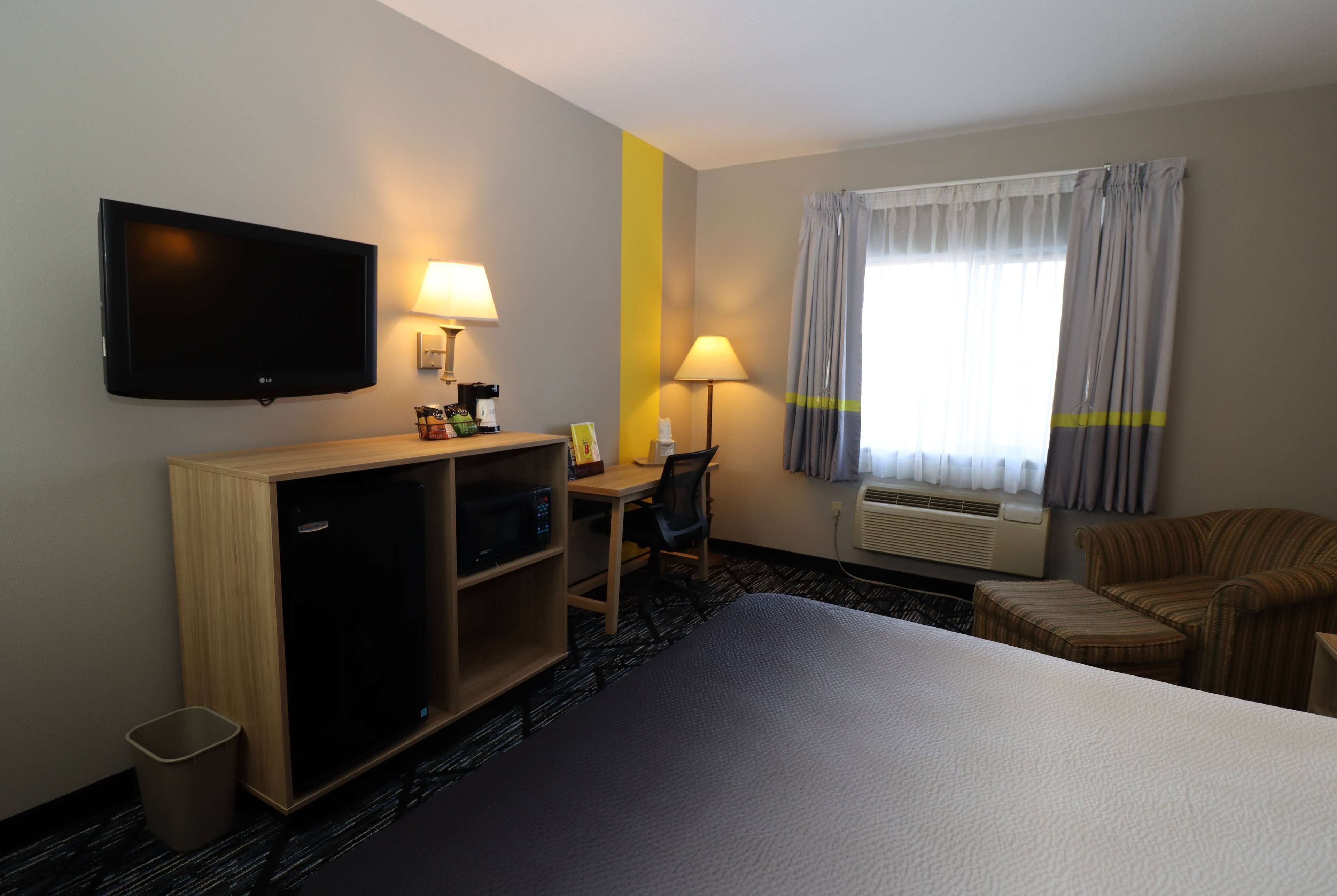 A hotel room with a bed, desk, chair, TV, lamp, and air conditioning unit.