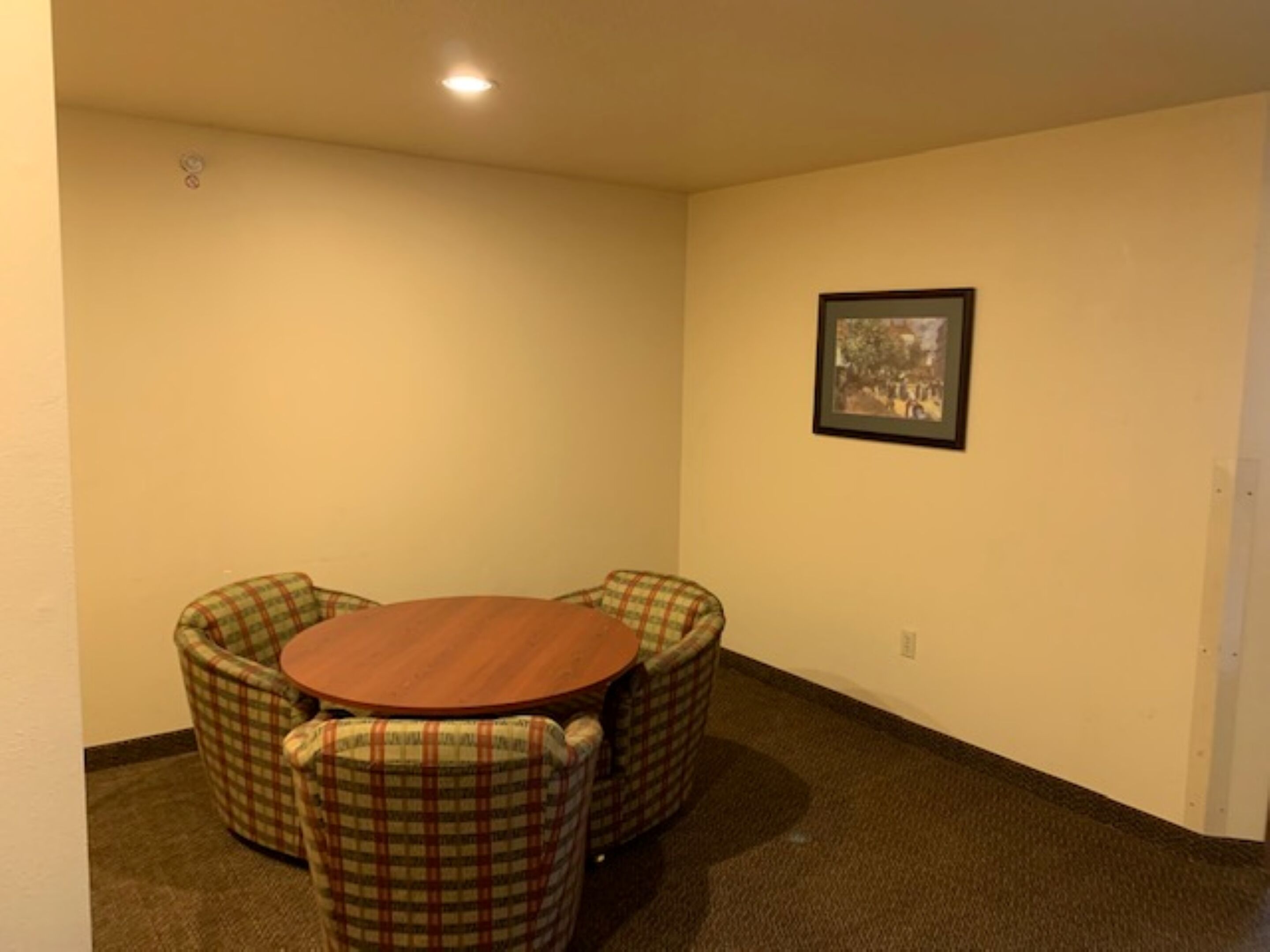 A small, carpeted room with a round table and four plaid chairs.