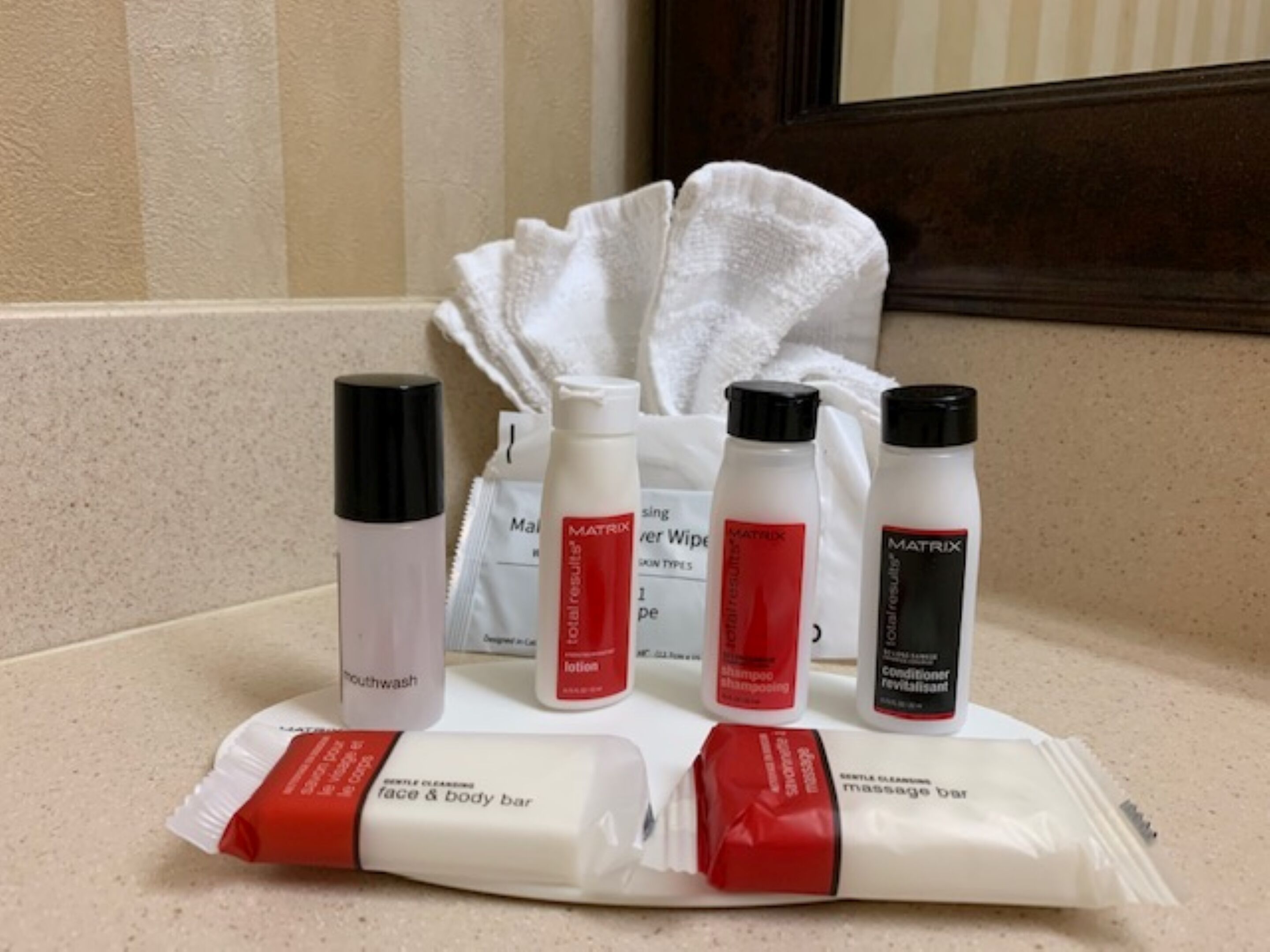 Una encimera de baño con diversos productos de cuidado personal, incluyendo pastillas para el rostro y el cuerpo, enjuague bucal y productos de la marca Matrix.