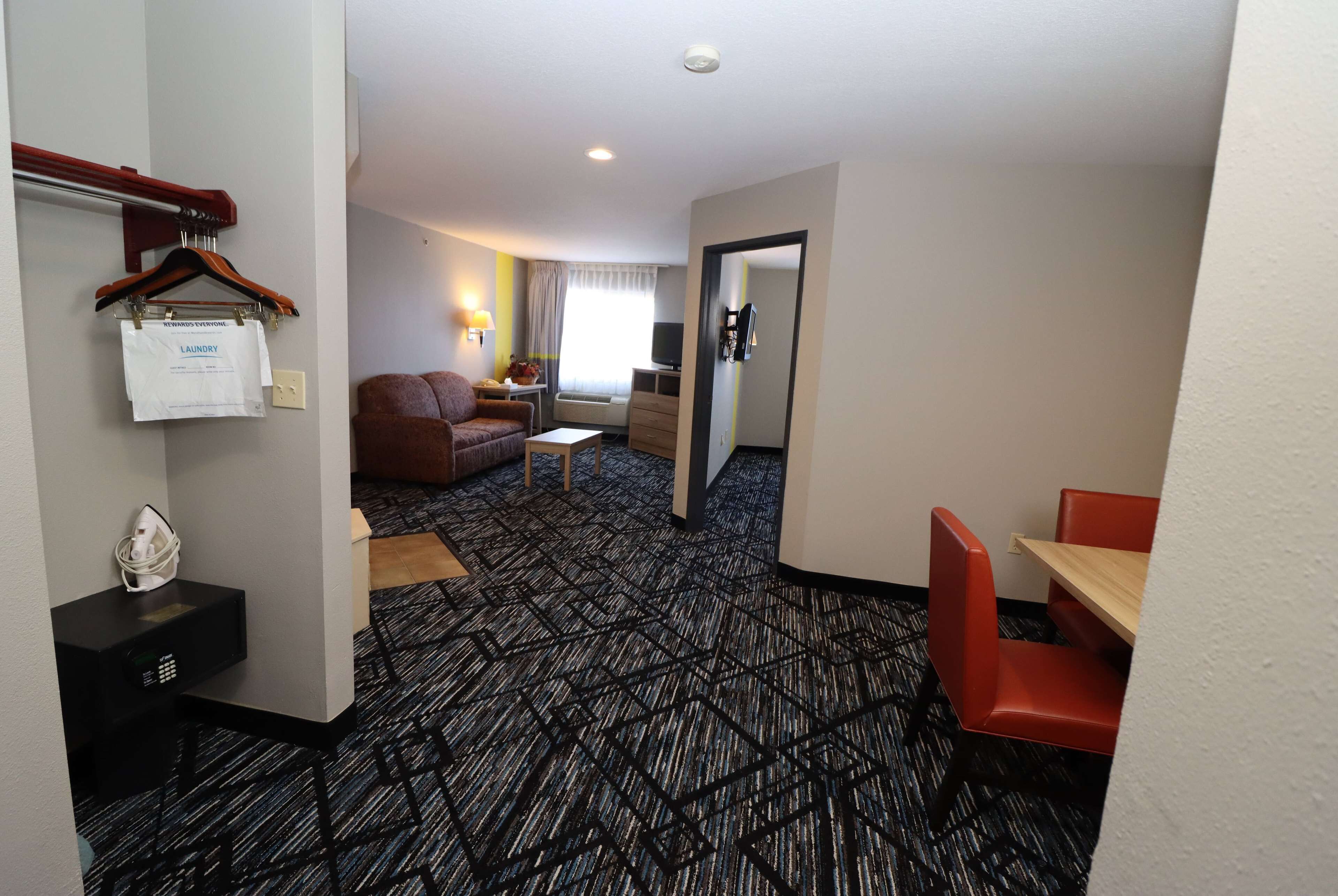 Una habitación de hotel con alfombra estampada, un sofá, una mesita, un televisor y un espejo.