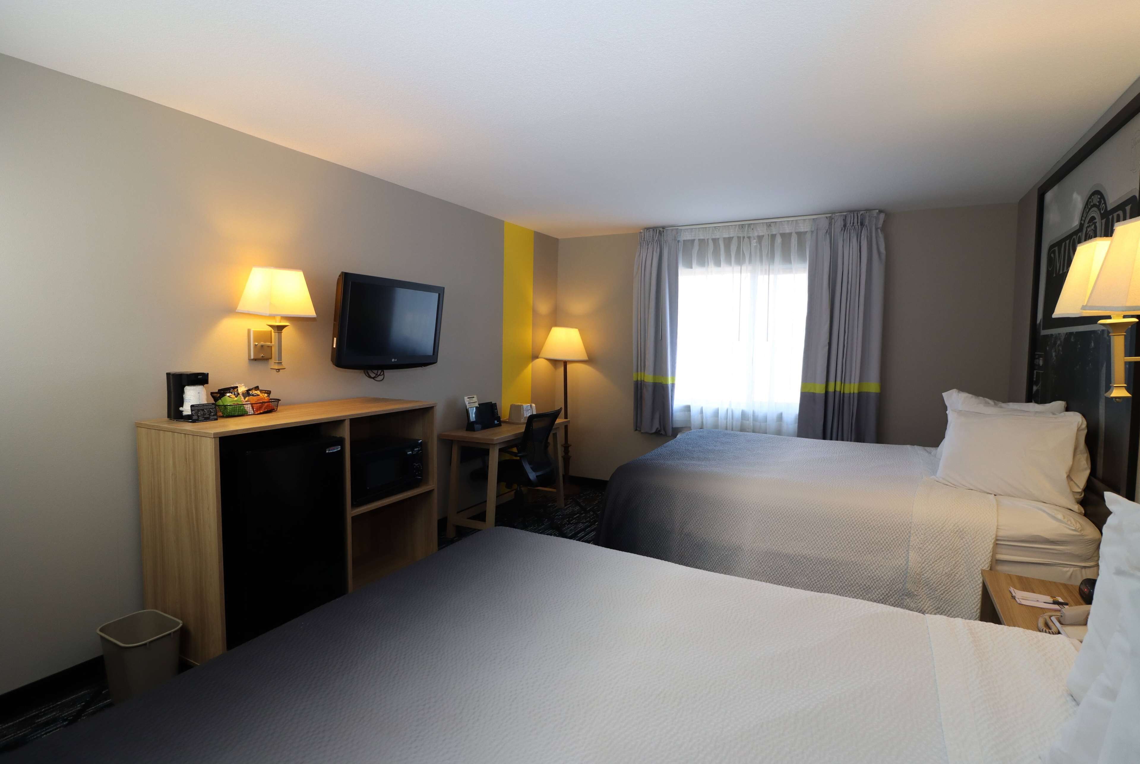 A hotel room with two beds, a desk, a television, and a window with curtains.