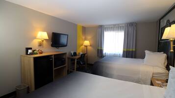 A hotel room with two beds, a desk, a television, and a window with curtains.