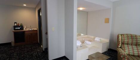 A hotel room with a kitchenette, a large mirror, a sofa, and a patterned carpet.