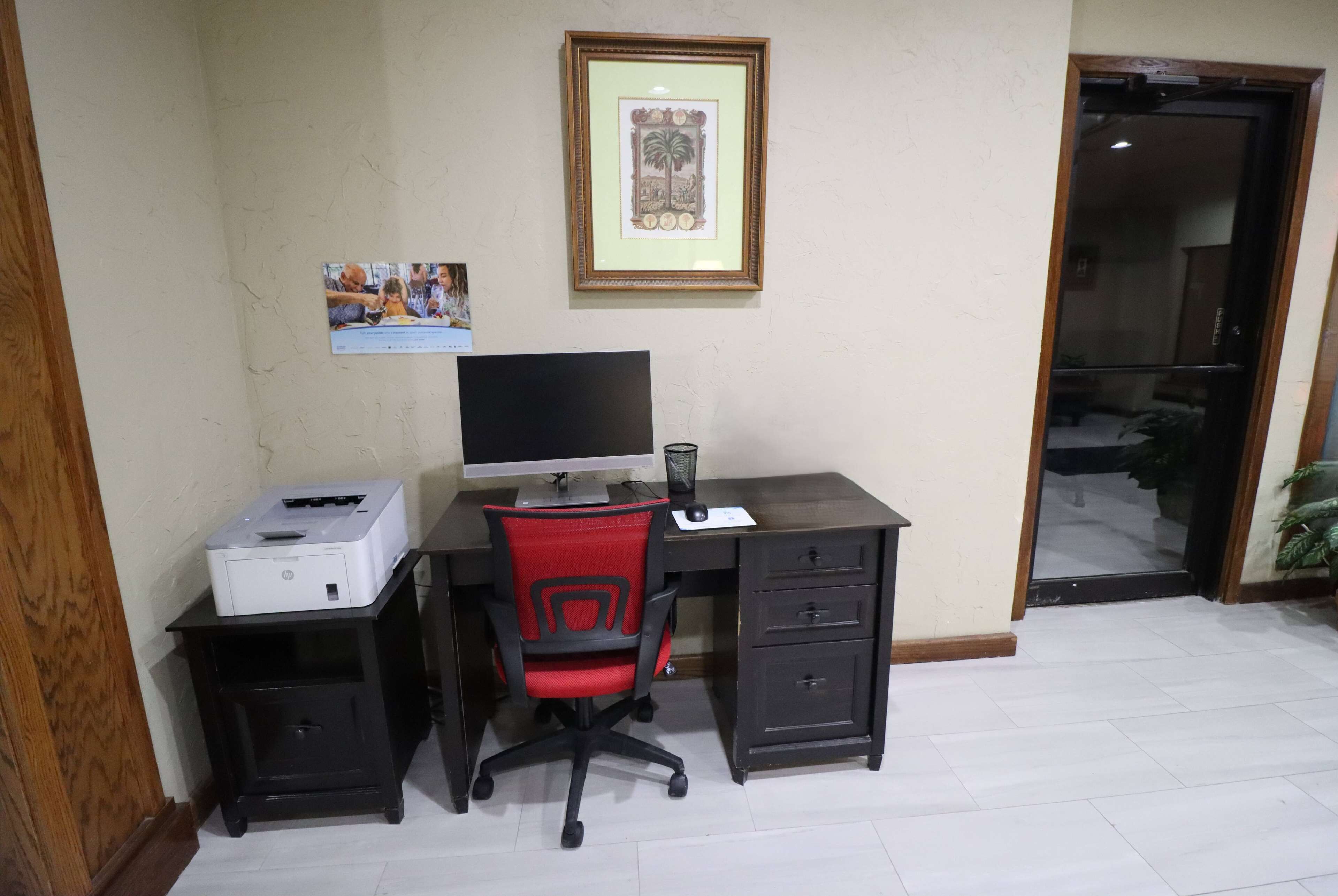 A home office setup with a desk, chair, computer, printer, and framed pictures on the wall.