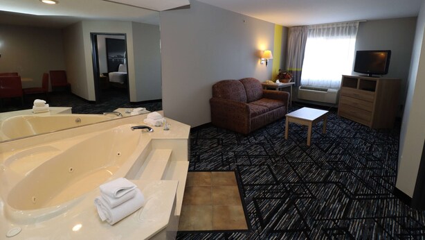 Une chambre d’hôtel avec une grande baignoire, un canapé, une petite table, une télévision et une fenêtre avec des rideaux.