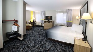 Une chambre d’hôtel avec un grand lit, un bureau avec une chaise, une télévision et une petite table avec une lampe.