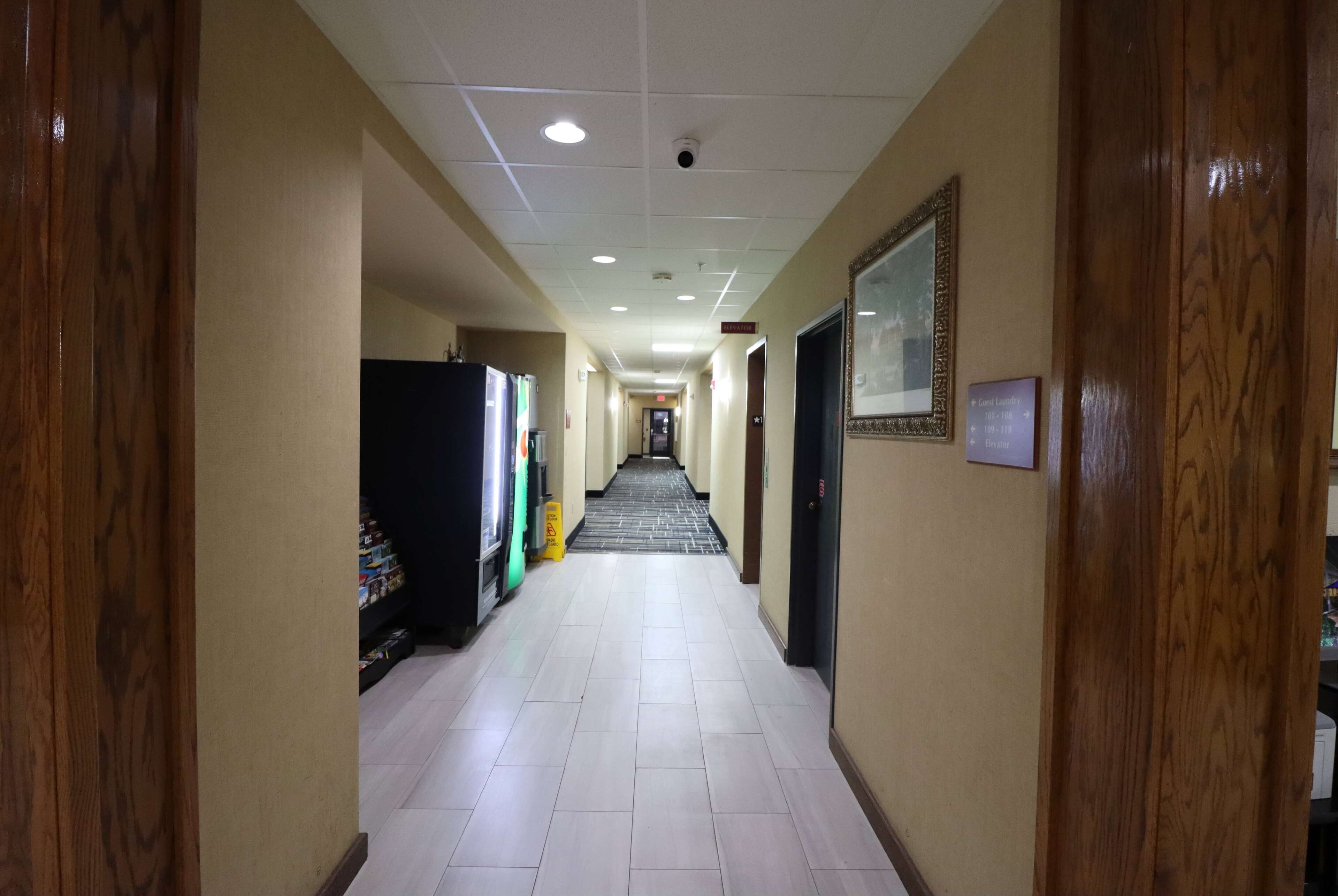 Un corridoio d'hotel con pavimento piastrellato, pannelli di legno alle pareti, una macchina per distributore e un quadro appeso.