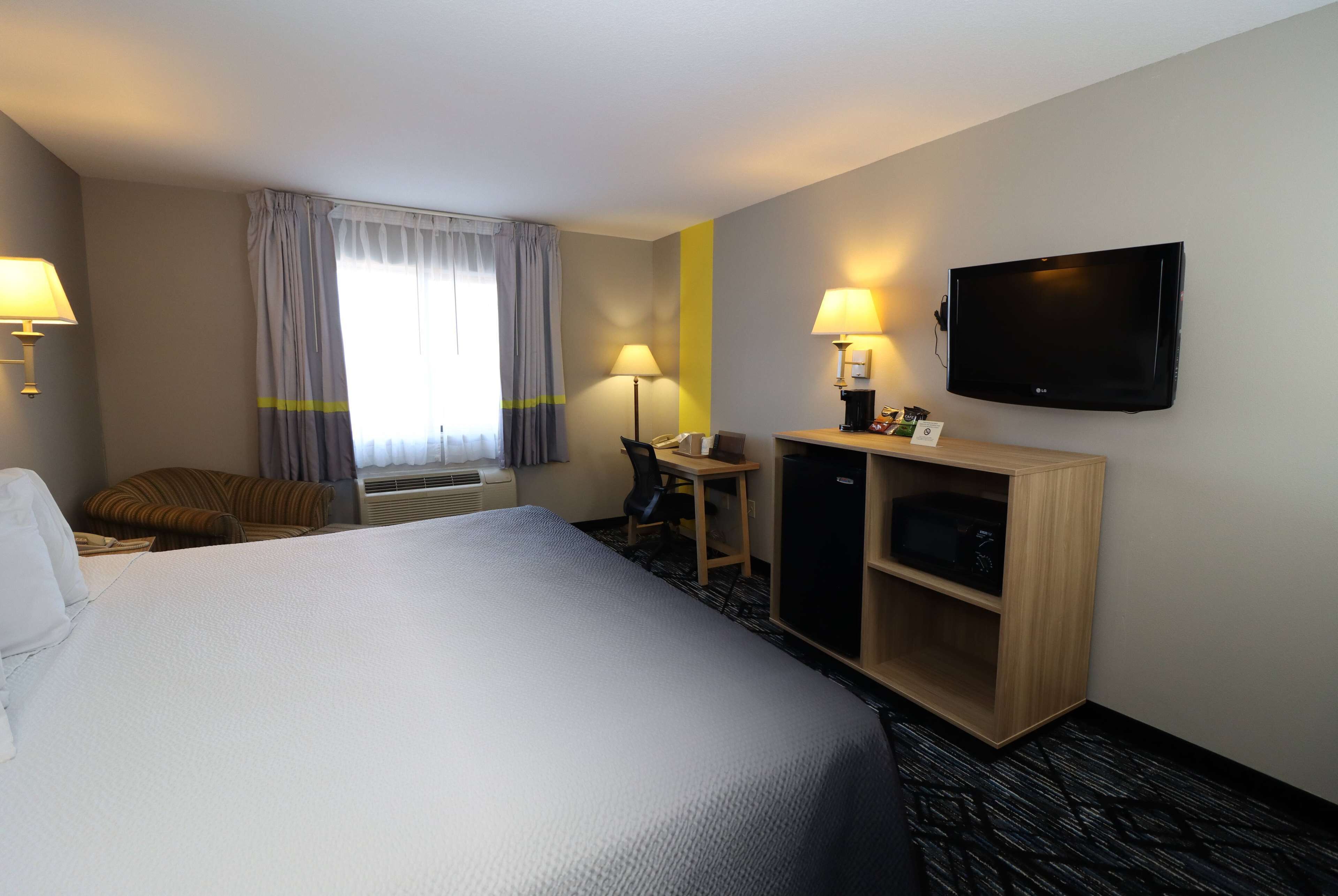 Een hotelkamer met een groot bed, een bureau, een stoel, een televisie en een kledingkast.