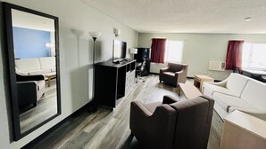 Ein modernes Hotelzimmer mit einem großen Spiegel, einem Flachbildfernseher, einem Schreibtisch, einem Sessel und einer Couch.