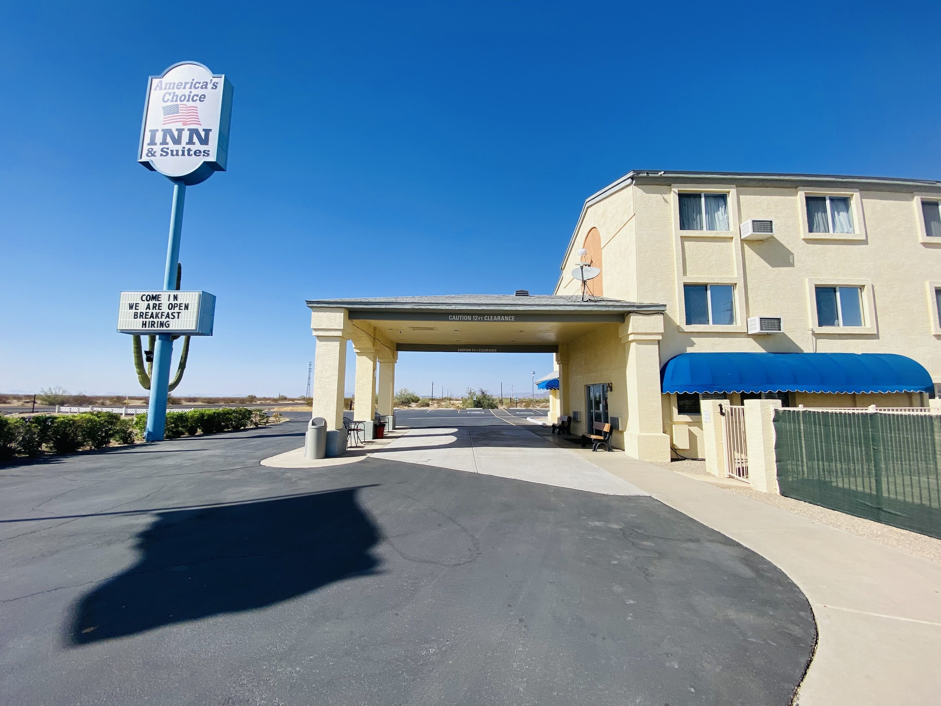 An American's Choice INN & Suites with a clear sky, a covered parking area, and a 12ft clearance sign.