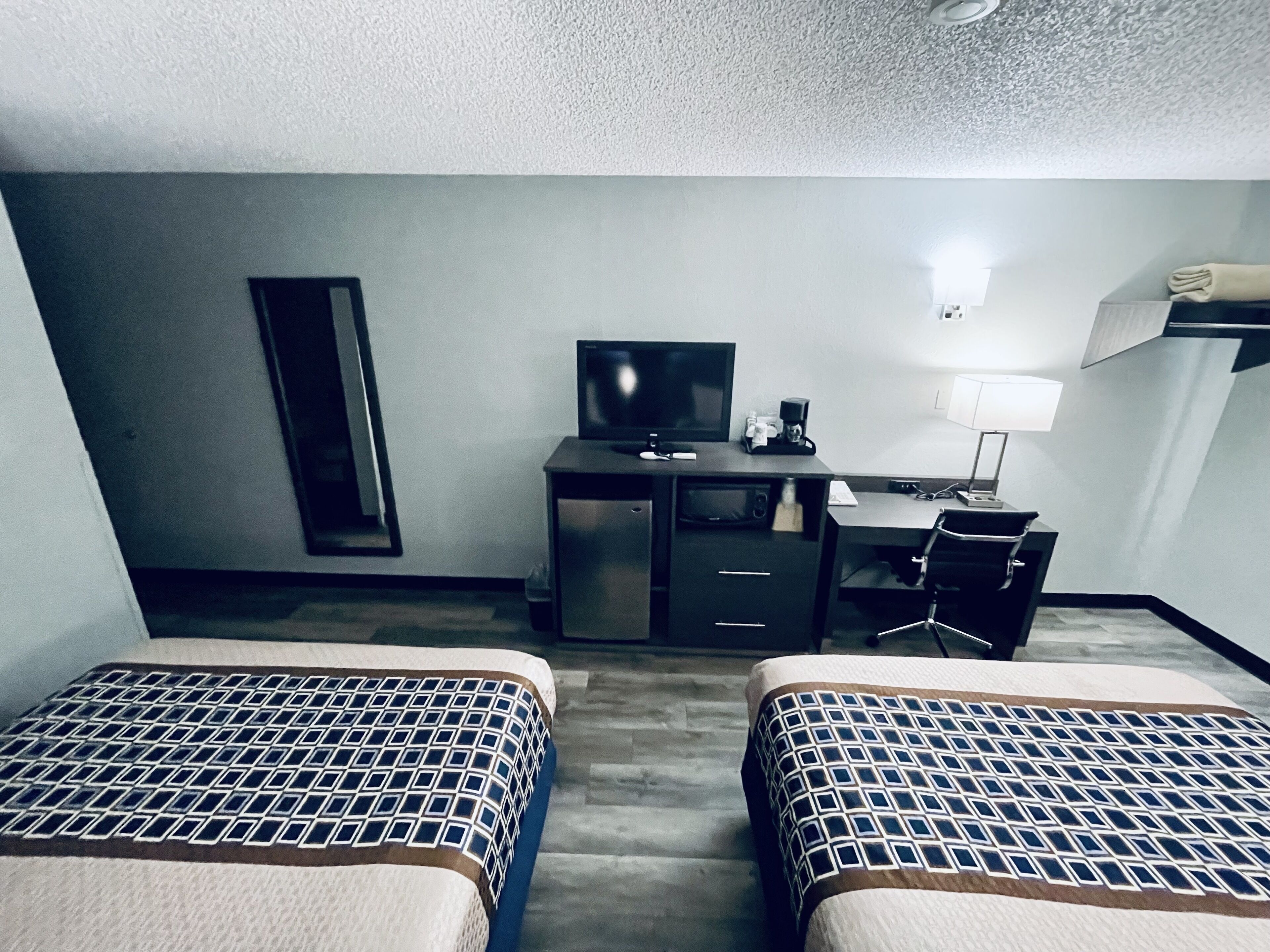 A hotel room with two beds, a desk with a TV, a lamp, and a chair.