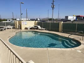 Una piscina con una escalera, sillas de descanso y un letrero de precaución.