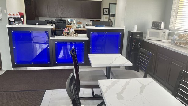 Eine moderne Küche mit dunklen Holzausziehtüren, einer blauen Akzentwand und einer weißen Marmorarbeitsplatte. Zwei weiße Tische mit Stühlen, eine Mikrowelle und eine Kaffeemaschine sind vorhanden.