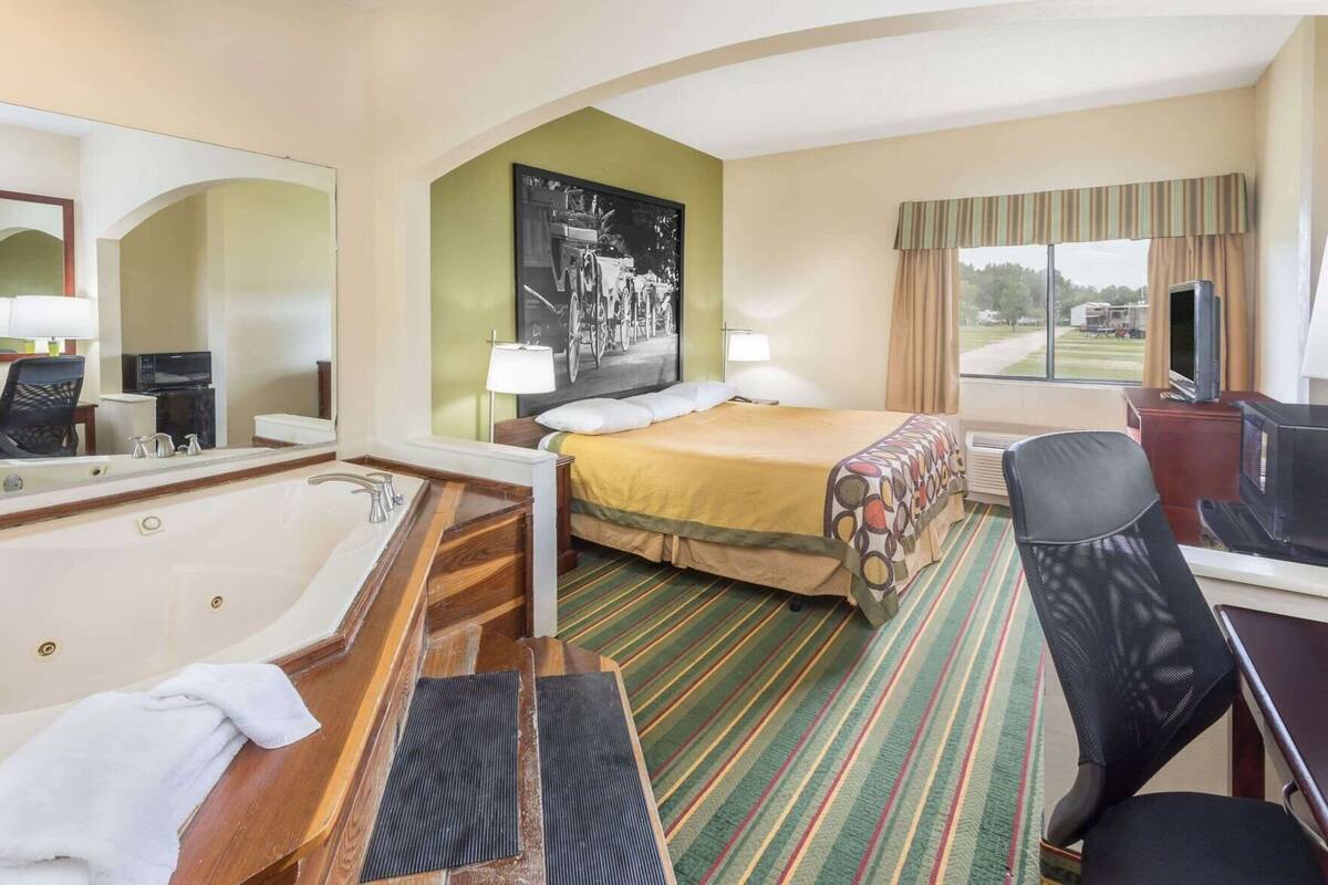 Een hotelkamer met een groot bed, een aparte badkamer met een badkuip, een bureau met een televisie, en een raam met uitzicht op de omgeving.