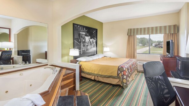 A hotel room with a large bed, a sitting area with a desk and chair, a bathtub, and a television. - Super 8 by Wyndham Duson Lafayette West Area (Duson)